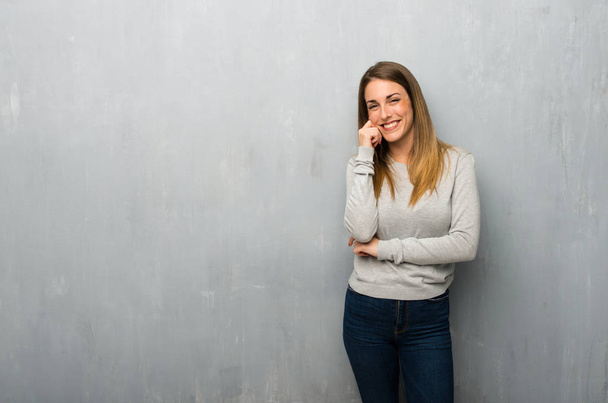 Jeune femme sur un mur texturé souriant avec une expression douce
 - Photo, image