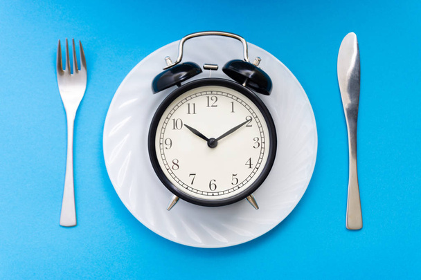 Ρολόι-ξυπνητήρι με πιρούνι και μαχαίρι στο τραπέζι. Ώρα για φαγητό, πρωινό, Μεσημεριανό η έννοια του χρόνου και το δείπνο. - Φωτογραφία, εικόνα