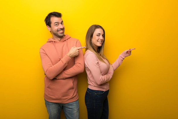 Group of two people on yellow background pointing finger to the side in lateral position - Photo, Image
