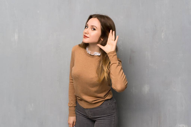 Teenager Mädchen über texturierter Wand hört etwas, indem sie die Hand auf das Ohr legt - Foto, Bild