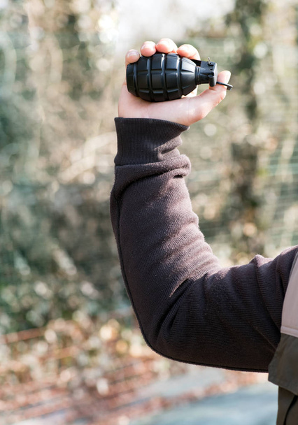 Homme posant pour lancer une grenade levant la main en l'air avec l'anneau de la broche accroché sur son pouce dans un concept de guerre ou de terrorisme
 - Photo, image