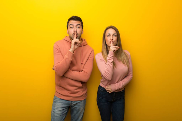 Csoport-a két ember a sárga háttér mutató ujj amivel szájban csend gesztus jele - Fotó, kép