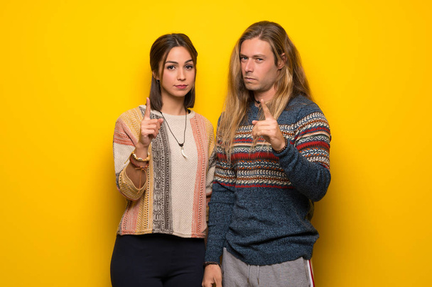 Hippie pareja sobre amarillo fondo frustrado por una mala situación y señalando a la parte delantera
 - Foto, imagen