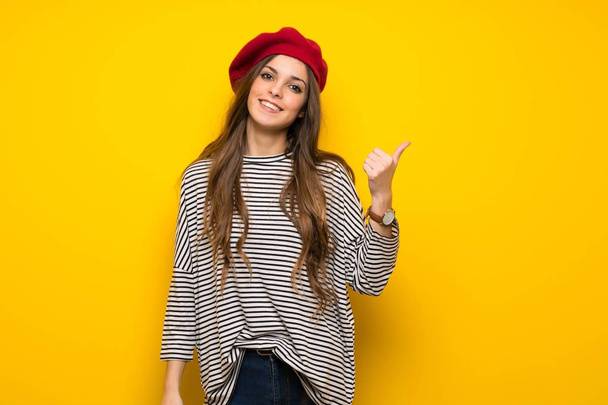 Girl with french style over yellow wall pointing to the side to present a product - 写真・画像