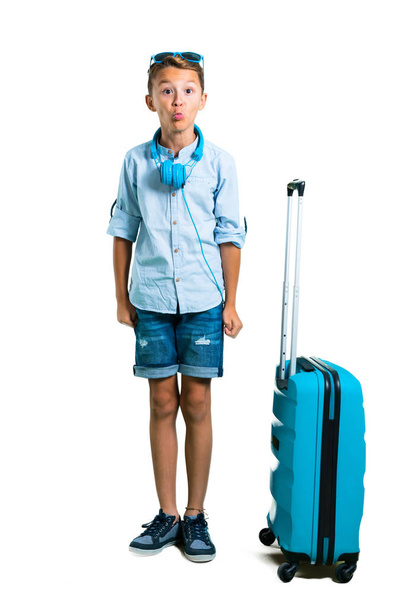 Full body of Kid with sunglasses and headphones traveling with his suitcase makes funny and crazy face emotion on isolated white background - Photo, Image