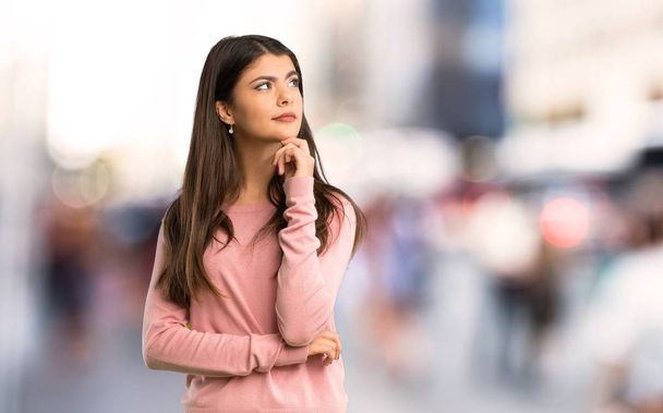Tiener meisje met roze shirt op zoek naar de kant met de hand op de kin in city - Foto, afbeelding