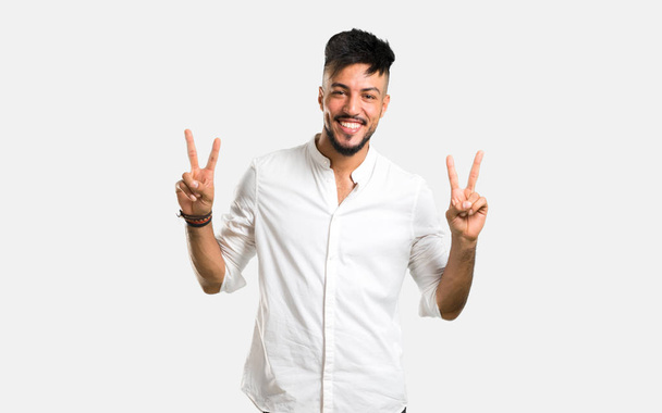 Arabo giovane uomo con camicia bianca sorridente e mostrando segno di vittoria su sfondo grigio
 - Foto, immagini