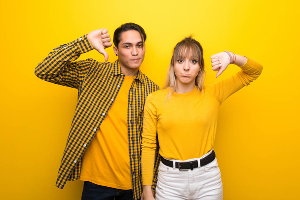 Fiatal pár több mint élénk sárga háttér mutatja hüvelykujját le mindkét kezével - Fotó, kép