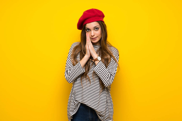 Dziewczyna z francuskim stylu na żółtej ścianie utrzymuje palm razem. Osoba prosi o coś - Zdjęcie, obraz