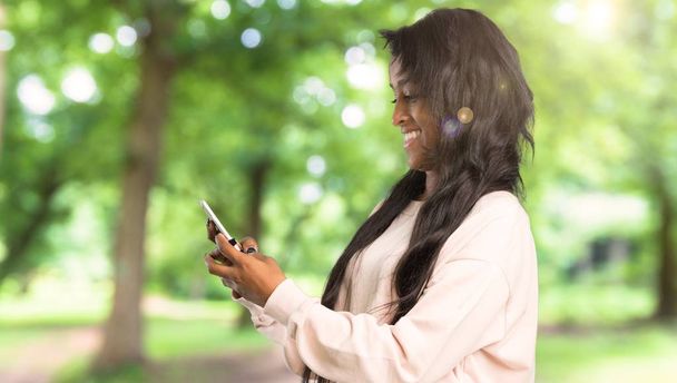 屋外で携帯電話でメッセージを送信する若いアフロ ・ アメリカ人女性 - 写真・画像