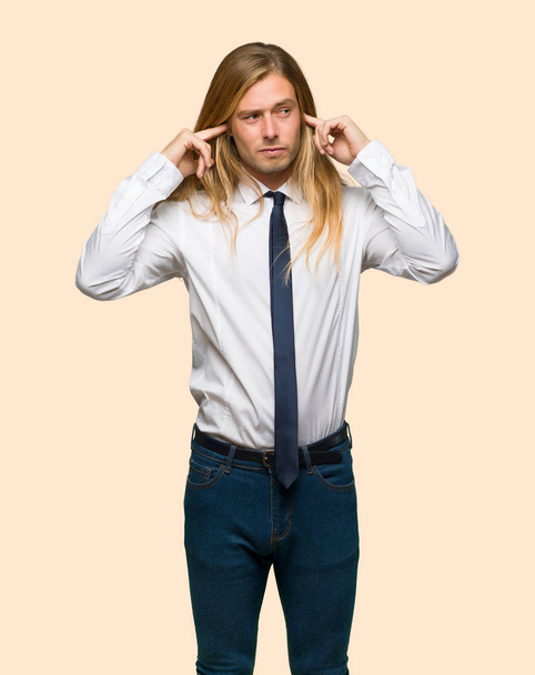 Blond businessman with long hair covering both ears with hands on isolated background - Fotografie, Obrázek