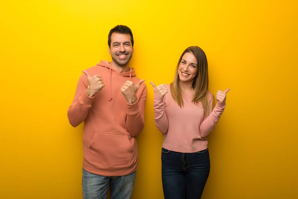 Groupe de deux personnes sur fond jaune donnant un geste pouce levé avec les deux mains et souriant
 - Photo, image