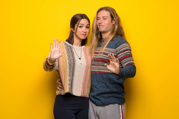 Hippie ζευγάρι πάνω από το κίτρινο φόντο είναι λίγο νευρικό και φοβισμένος, τεντώνοντας τα χέρια προς τα εμπρός - Φωτογραφία, εικόνα