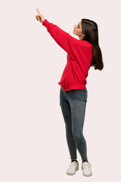 Una toma completa de una adolescente con suéter rojo apuntando hacia un fondo aislado
 - Foto, Imagen