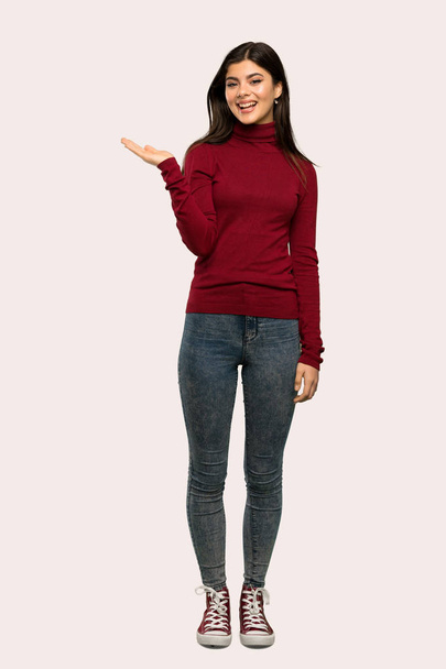 A full-length shot of a Teenager girl with turtleneck holding copyspace imaginary on the palm to insert an ad over isolated background - Zdjęcie, obraz