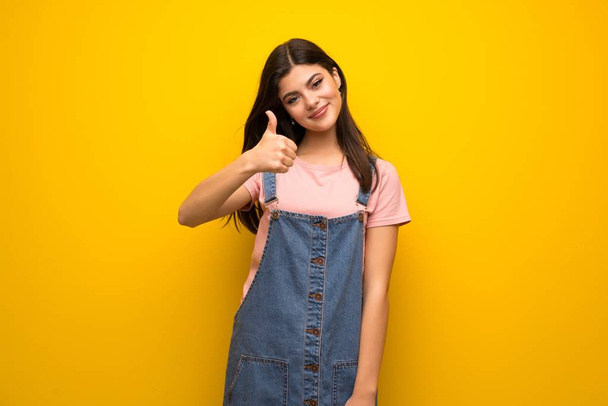Teenager girl over yellow wall with thumbs up because something good has happened - Фото, изображение