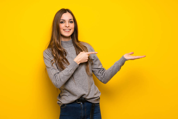 Mladá žena nad žluté zdi drží imaginární copyspace na dlani vložit inzerát - Fotografie, Obrázek