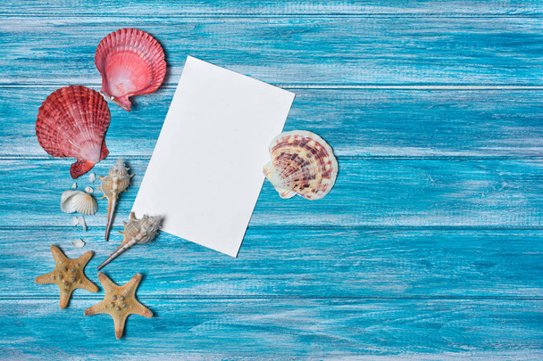 Top view on mock-up of white paper card for photo or lettering with starfish and seashells on blue wooden background with copy space - Foto, Imagen