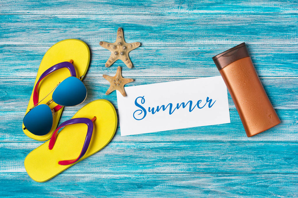 Top view on bright yellow flip flops with sunglasses and sunscreen as concept of vacation time on blue wooden background - Fotografie, Obrázek