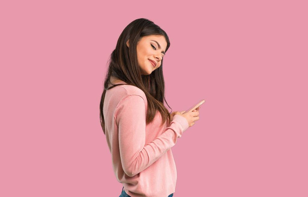 Menina adolescente com camisa rosa enviando uma mensagem com o celular no fundo rosa isolado
 - Foto, Imagem