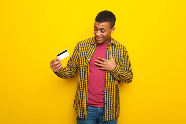 Giovane afro americano su sfondo giallo in possesso di una carta di credito e sorpreso
 - Foto, immagini