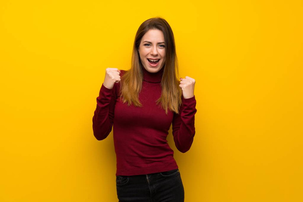 Woman with turtleneck over yellow wall celebrating a victory in winner position - Photo, Image