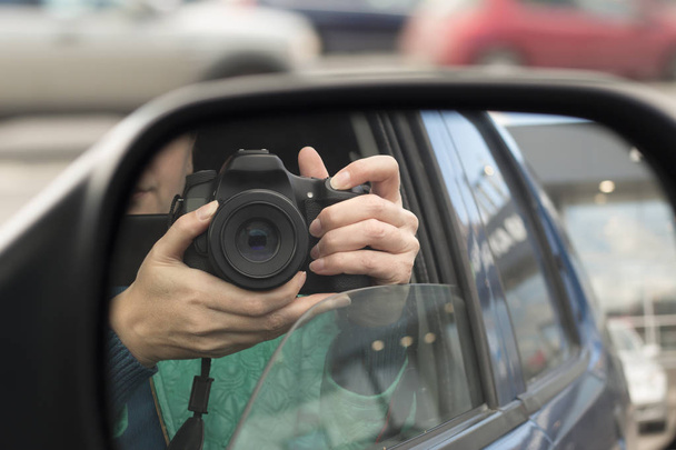 Hidden photographing. Reflection in car mirror of woman with camera. Paparazzi concept - Zdjęcie, obraz