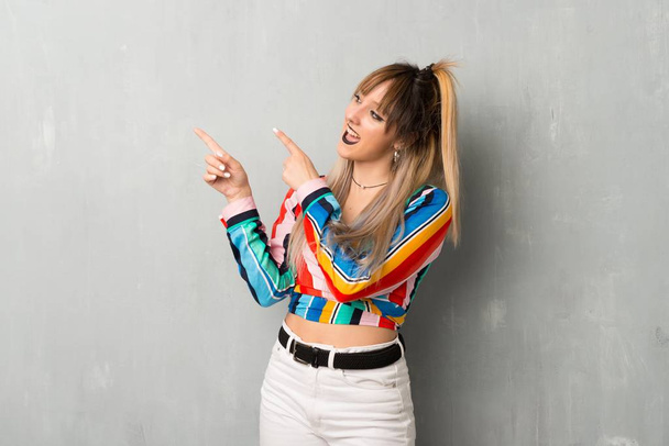 Молода дівчина з барвистим одягом, що вказує на індексний палець і дивиться вгору
 - Фото, зображення