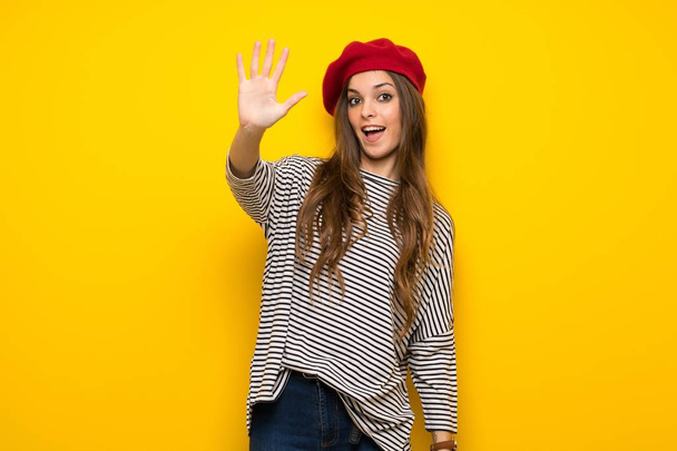 Girl with french style over yellow wall counting five with fingers - Foto, afbeelding