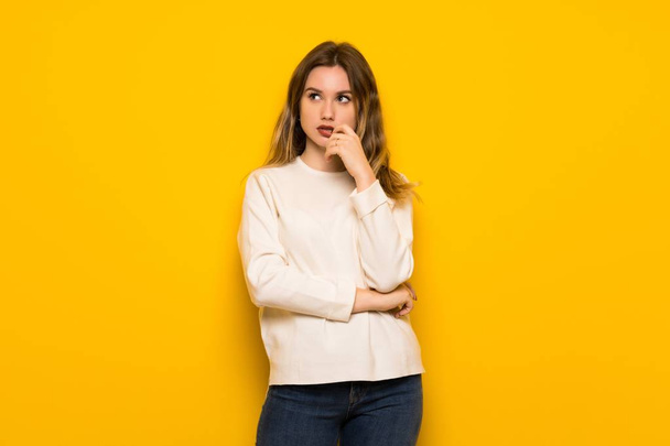 Teenager girl over yellow wall having doubts while looking up - Photo, Image