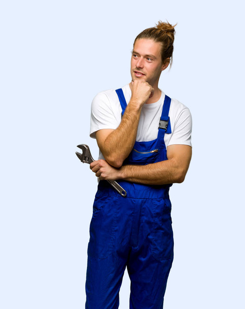 Рабочий смотрит в сторону с рукой на подбородке на изолированном фоне
 - Фото, изображение