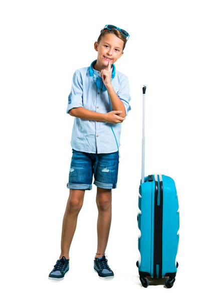 Full body of Kid with sunglasses and headphones traveling with his suitcase laughing on isolated white background - Photo, Image