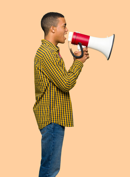 Young afro american man shouting through a megaphone to announce something in lateral position on isolated background - Foto, afbeelding