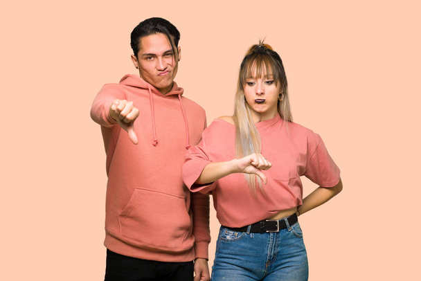 Молодая пара показывает знак вниз большого пальца с негативным выражением на розовом фоне
 - Фото, изображение