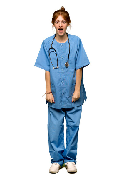 Uma foto completa de uma enfermeira ruiva jovem com expressão facial surpresa e chocada sobre fundo branco isolado
 - Foto, Imagem