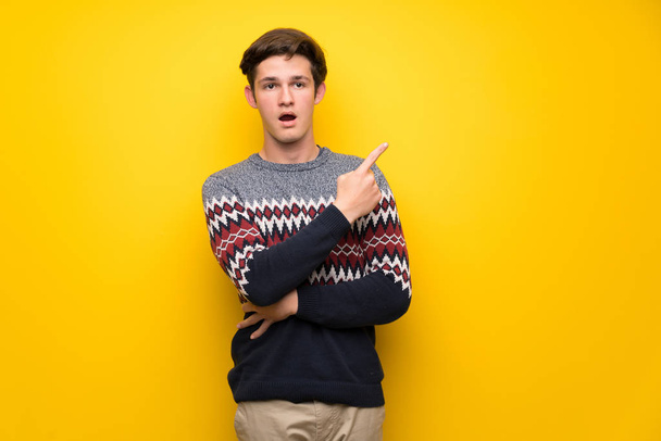 Teenager man over yellow wall surprised and pointing side - Photo, Image