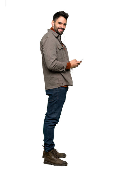 Celovečerní snímek pohledný muž s plnovousem, odesláním zprávy s mobilním telefonem na izolované bílém pozadí - Fotografie, Obrázek