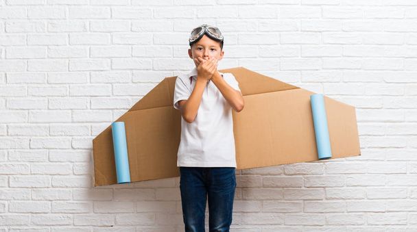 Хлопчик грає з картонними крилами літака на спині, покриваючи рот руками
 - Фото, зображення