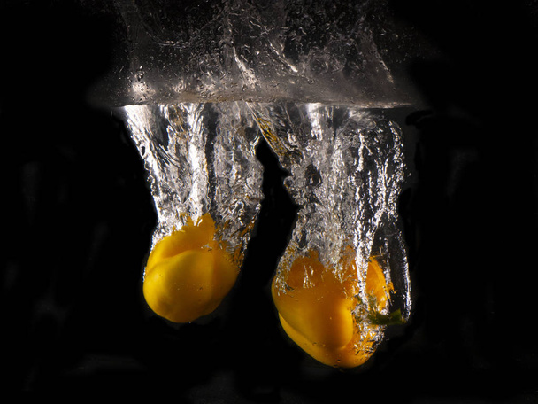 yellow Bell pepper falling into splashing water on black background - Fotoğraf, Görsel
