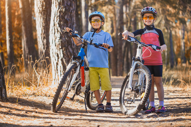 kids on abicycles in the sunny forest.happy children cycling outdoors in helmet - Fotografie, Obrázek