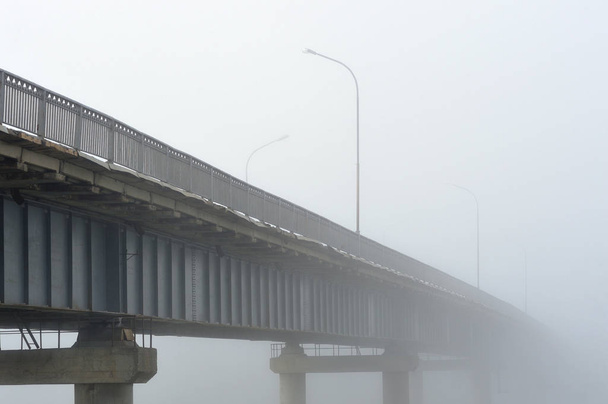 Pont au-dessus de la rivière pendant un brouillard matinal dense disparaissant en elle
. - Photo, image