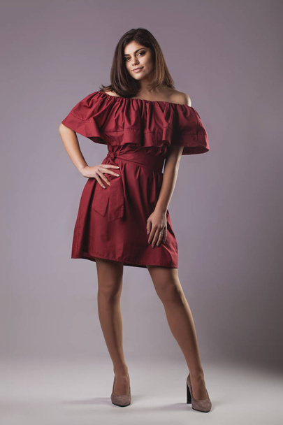Young brunette woman in red dress posing on grey background - Foto, immagini