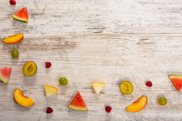 Pieces of fruit, apple, peach, melon, watermelon, grapes, plum, raspberry, lie on a textured light wooden background. Flat top view, place for text. Flat Lay, Copy Space. Summer background. - Photo, Image