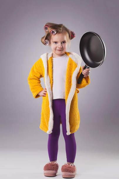 a small hostess in a dressing gown with a frying pan. Studio photo - Zdjęcie, obraz
