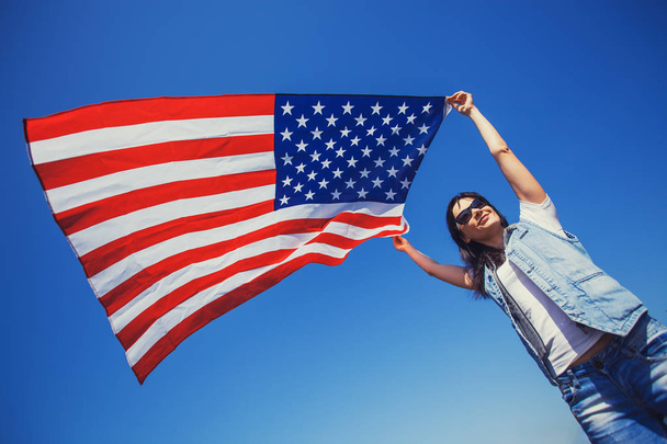 happy smiling young woman with national american flag against the blue sky. Independence Day, 4th July - 写真・画像