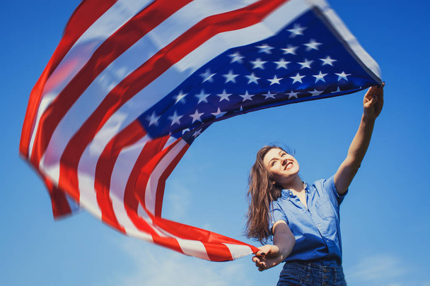 happy smiling young woman with national american flag against the blue sky. Independence Day, 4th July - Zdjęcie, obraz