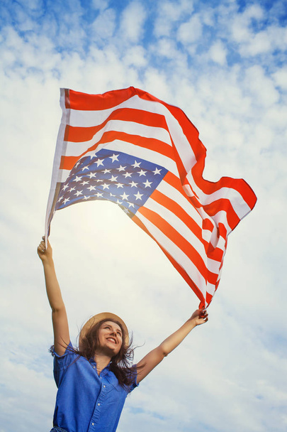 happy smiling young woman with national american flag against the blue sky. Independence Day, 4th July - 写真・画像