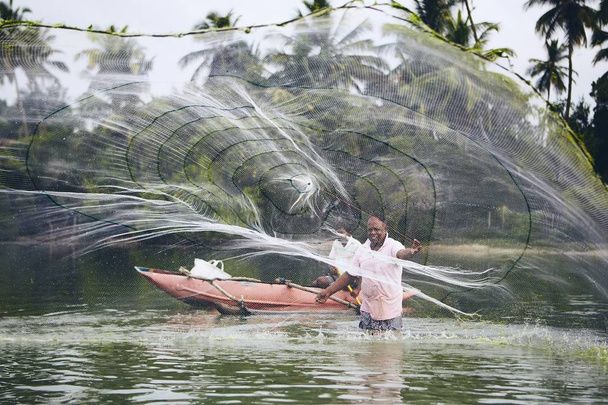 Fisherman is throwing fishing net on lake against beach with palm trees in Sri Lanka.   - Photo, Image