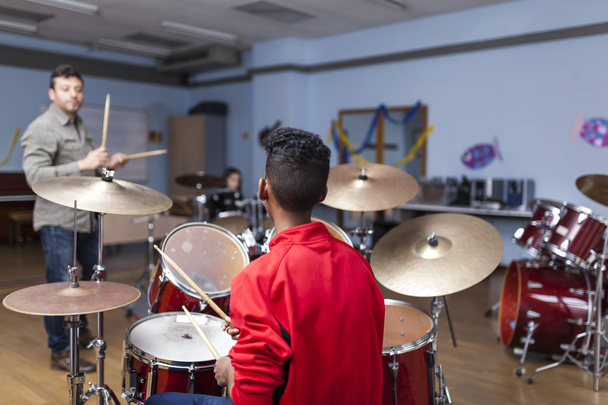 Unrecognizable Afro boy with red jacket attending a drum class, back view - Fotó, kép