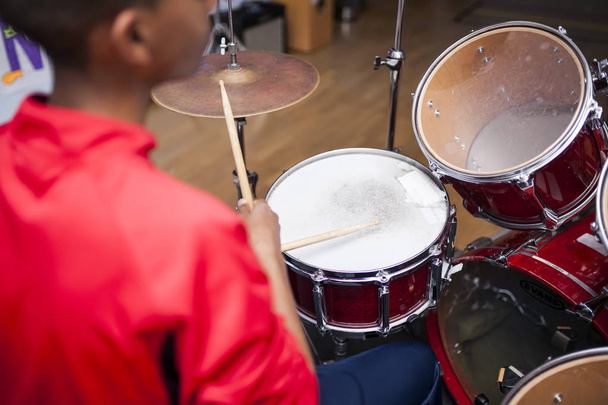 Unrecognizable Afro boy with red jacket attending a drum class, back view - Foto, Imagen